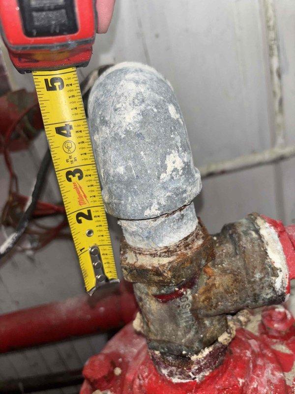 Performed site visit to assess water service issue where occupants had no water supply and were unable to use facilities. Inspection revealed significant corrosion and mineral buildup at connection points between the red painted pipes and PVC components of the water system. Documented extensive deterioration at pipe joints with visible rust and water damage to surrounding wall areas; determined city needs to replace shut-off at meter vault before further repairs can proceed.