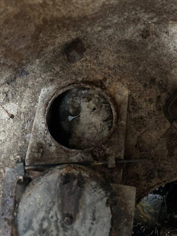 Conducted inspection of severely corroded commercial drainage system with significant deterioration. Documented extensive rust damage, mineral buildup, and complete blockage in circular pipe opening embedded in concrete. Photographic evidence captured to document condition of aged mechanical components requiring replacement as sold by service team.