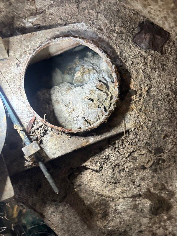 Conducted inspection of severely corroded commercial drainage system with significant deterioration. Documented extensive rust damage, mineral buildup, and complete blockage in circular pipe opening embedded in concrete. Photographic evidence captured to document condition of aged mechanical components requiring replacement as sold by service team.