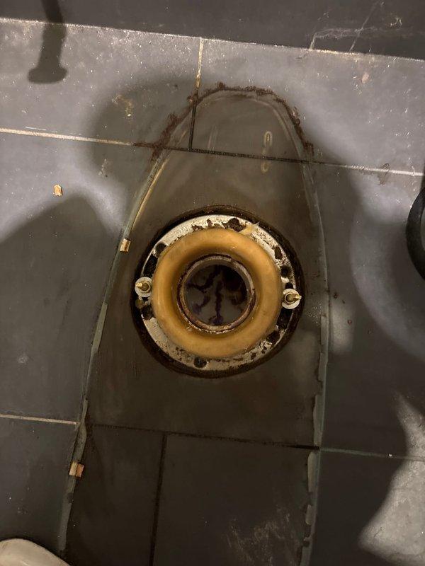 Responded to a second-floor toilet leak affecting the first-floor living room. Inspection revealed a deteriorated wax ring seal at the toilet base with visible staining and water damage. Observed significant corrosion and mineral buildup around the drain fixture with evidence of prolonged water exposure.