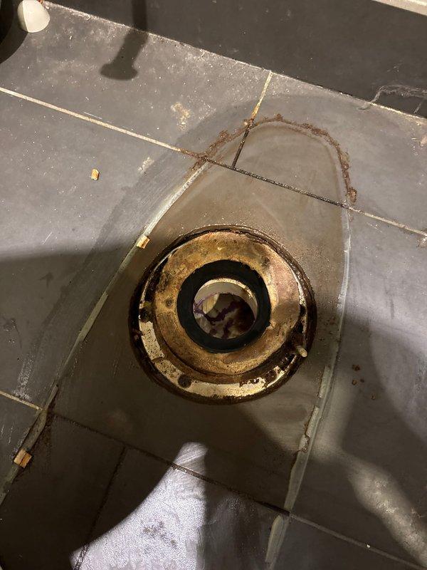 Responded to a second-floor toilet leak affecting the first-floor living room. Inspection revealed a deteriorated wax ring seal at the toilet base with visible staining and water damage. Observed significant corrosion and mineral buildup around the drain fixture with evidence of prolonged water exposure.