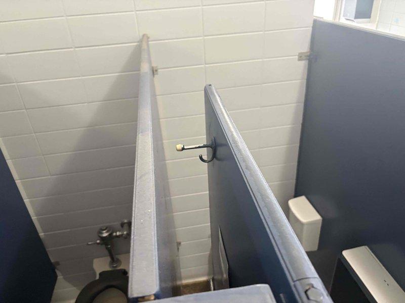 Conducted site assessment of commercial bathroom renovation project involving conversion of 12 toilet stalls to 10 stalls across two floors, with 5 wall-mounted sinks requiring replacement. Documented existing fixtures and partition configurations, noting standard commercial dividers with metal edges, commercial-grade toilets with wall-mounted flush valves, and brick-pattern white tile walls.