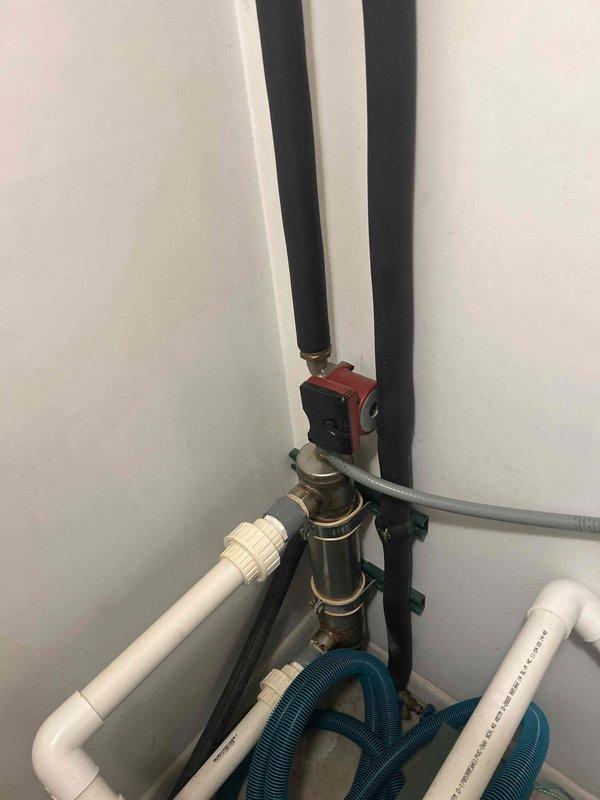 Completed inspection of basement sump pump installation with associated PVC drainage system. Documented condition of shutoff valve and pipe connections including the black insulated vertical pipes with red valve component. Verified proper installation of flexible drainage hose and all plumbing connections, with no visible leaks or deterioration observed in the utility area infrastructure.