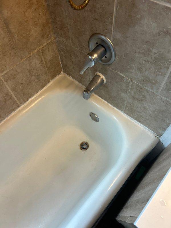 Responded to priority service call for shower leakage affecting downstairs unit in century-old building. Inspection revealed deteriorated grout and seal around tub/shower fixtures, with water penetrating through ceiling below. Removed damaged areas, applied professional-grade silicone sealant around all fixtures and tub perimeter, and verified proper drainage function to successfully resolve the leak.