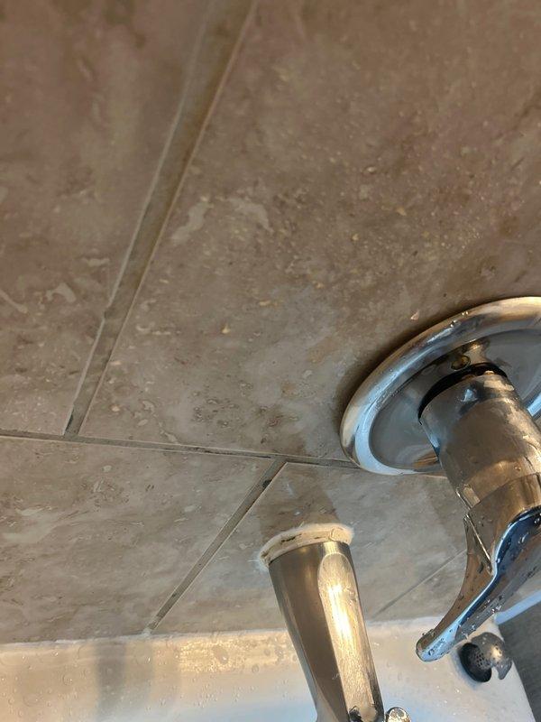Responded to priority service call for shower leakage affecting downstairs unit in century-old building. Inspection revealed deteriorated grout and seal around tub/shower fixtures, with water penetrating through ceiling below. Removed damaged areas, applied professional-grade silicone sealant around all fixtures and tub perimeter, and verified proper drainage function to successfully resolve the leak.