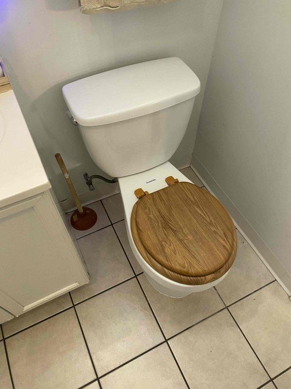 Replaced severely corroded toilet flange on tiled bathroom floor with new unit and reinstalled existing two-piece toilet with wooden seat. Verified proper seal and function of toilet after installation with no leaks present.