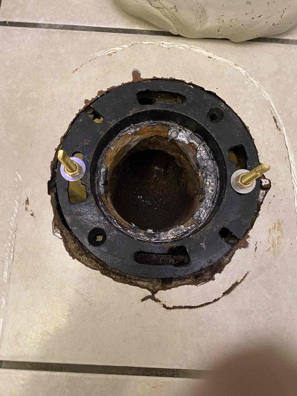 Replaced severely corroded toilet flange on tiled bathroom floor with new unit and reinstalled existing two-piece toilet with wooden seat. Verified proper seal and function of toilet after installation with no leaks present.