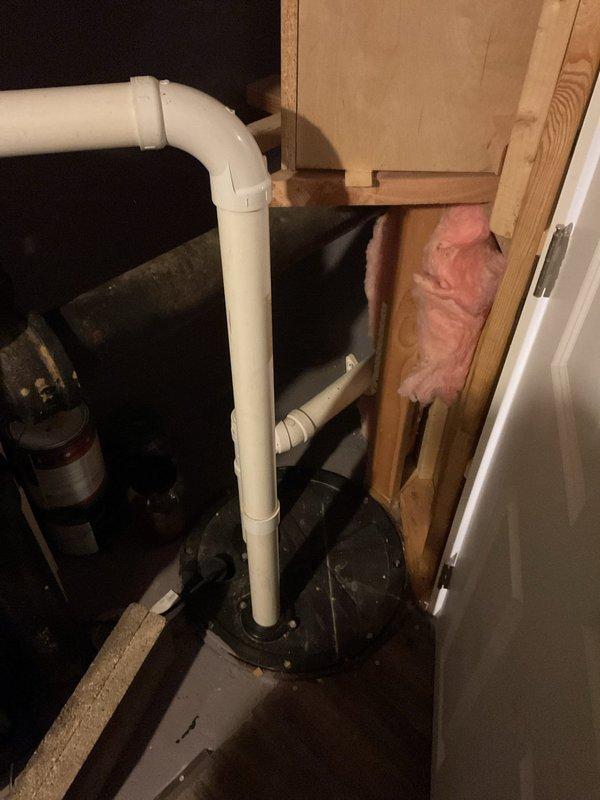 Conducted inspection of drainage system in commercial facility, focusing on PVC pipe installation connecting to sump pump basin. Observed existing configuration with vertical and horizontal PVC runs featuring a red shut-off valve. Documentation shows proper integration with building structure including proximity to wooden framing and insulation. Noted water present in the black sump basin, indicating active drainage system functionality.