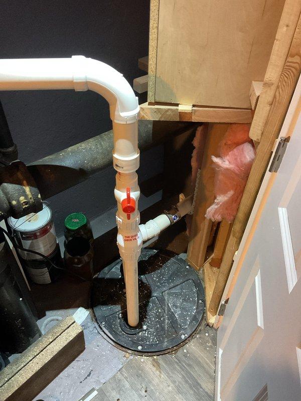 Conducted inspection of drainage system in commercial facility, focusing on PVC pipe installation connecting to sump pump basin. Observed existing configuration with vertical and horizontal PVC runs featuring a red shut-off valve. Documentation shows proper integration with building structure including proximity to wooden framing and insulation. Noted water present in the black sump basin, indicating active drainage system functionality.