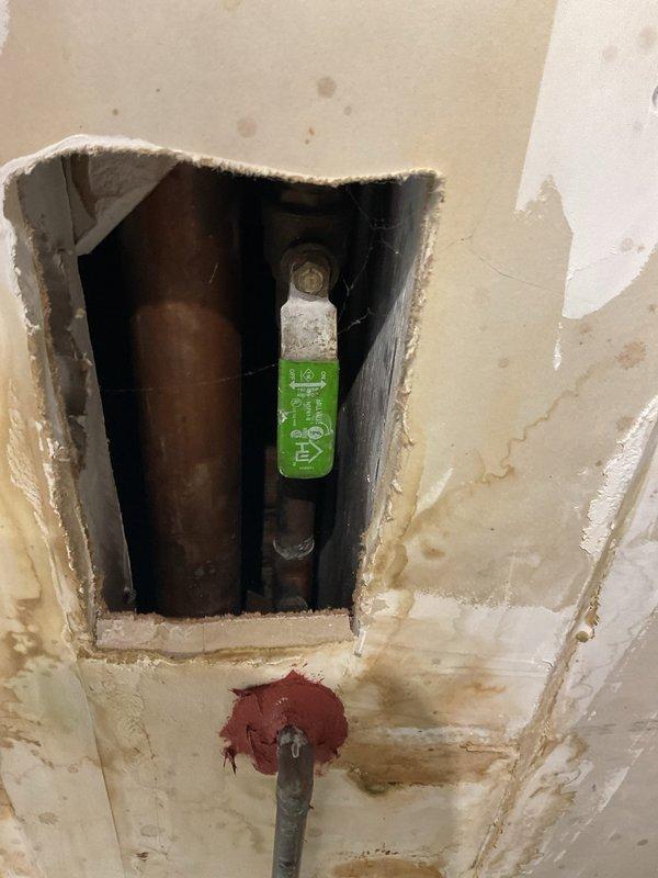 Responded to service call regarding floor drain backup and two problematic sinks. Upon inspection, discovered significant water damage around a wall access panel where a copper pipe with a green shut-off valve was visible. Further examination of the commercial kitchen area revealed exposed metal conduits and electrical wiring running along the ceiling, with evidence of unfinished drywall work suggesting previous plumbing issues. Cleared the floor drain obstruction and serviced both sink drains to restore proper drainage function.
