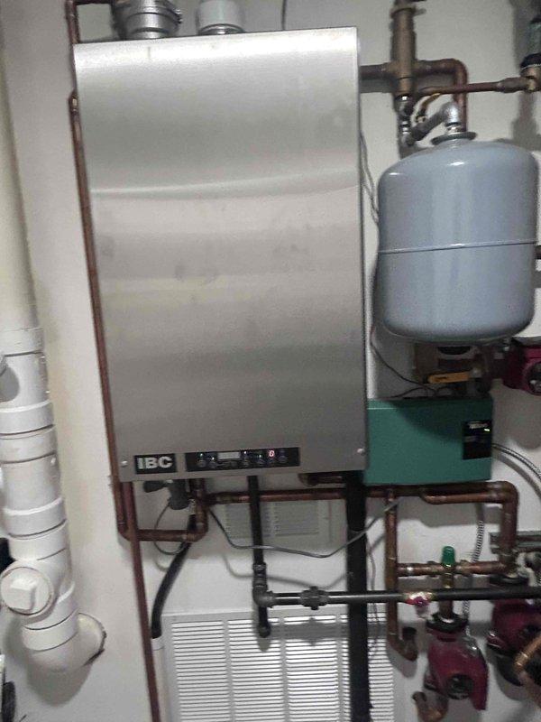 Responded to customer report of flies emanating from washer/dryer area and cross-connection issues causing hot/cold water mixing in kitchen and upstairs bathroom. Inspected mechanical room containing IBC boiler system with expansion tank, copper supply lines, and PVC drainage components. Visual assessment revealed no visible leaks or damage to the hydronic heating system that could be contributing to the reported plumbing issues.