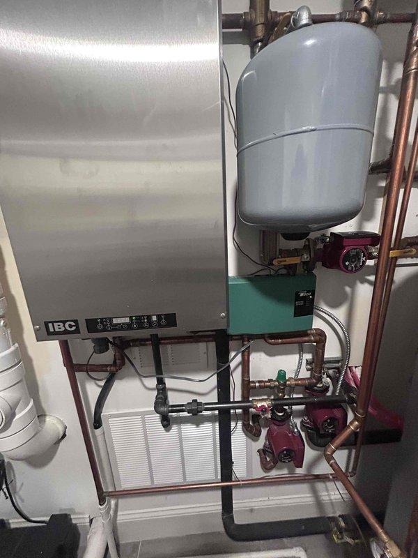 Responded to customer report of flies emanating from washer/dryer area and cross-connection issues causing hot/cold water mixing in kitchen and upstairs bathroom. Inspected mechanical room containing IBC boiler system with expansion tank, copper supply lines, and PVC drainage components. Visual assessment revealed no visible leaks or damage to the hydronic heating system that could be contributing to the reported plumbing issues.