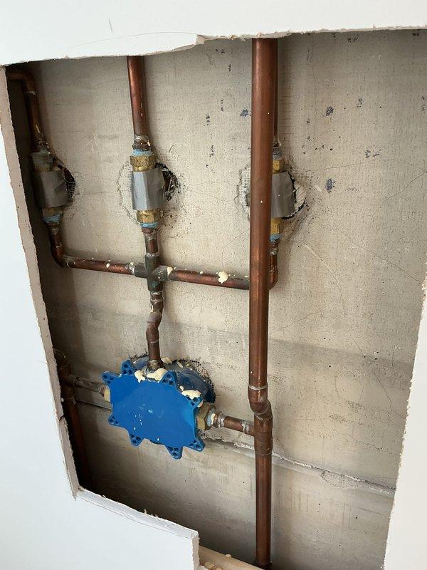 Responded to low water pressure complaint affecting shower fixtures. Upon inspection, discovered corroded and partially blocked supply pipes within wall cavity. Opened access point to replace deteriorated copper pipe sections and installed new shut-off valves to improve water flow. Tested both rainfall and wall-mounted shower fixtures after repair, confirming restoration of proper water pressure throughout the bathroom.
