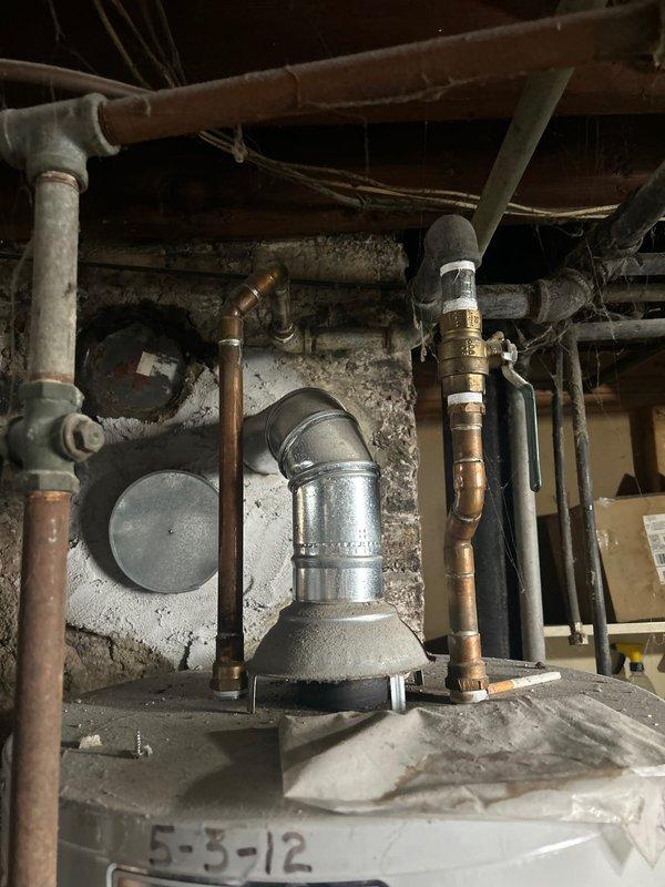 Completed inspection of an aging Bradford White water heater installed against brick wall with copper piping showing patina development. Observed existing installation including metallic vent pipe with elbow joint, brass valve connections, and proper ventilation components. Provided financing options for replacement of this unit which appears to be from 2012 based on visible date marking.