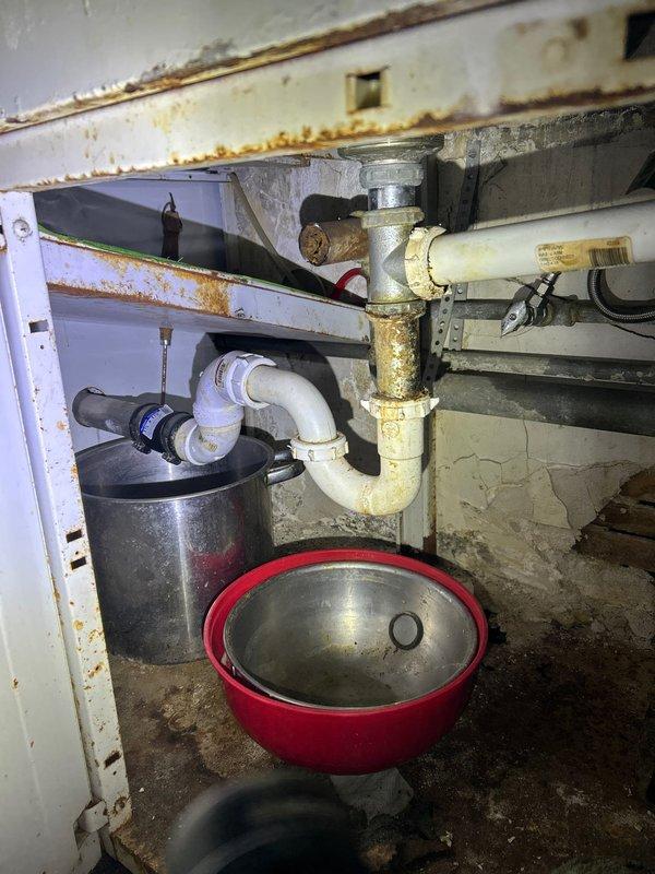 Located and diagnosed a ceiling leak originating from corroded metal drain pipes under a sink/basin in the room above. Discovered significant oxidation at pipe joints with visible moisture damage and rust stains throughout the cabinet area. Installed requested shut-off valve to address the slow drip that was penetrating the ceiling and causing water damage to the wall below.