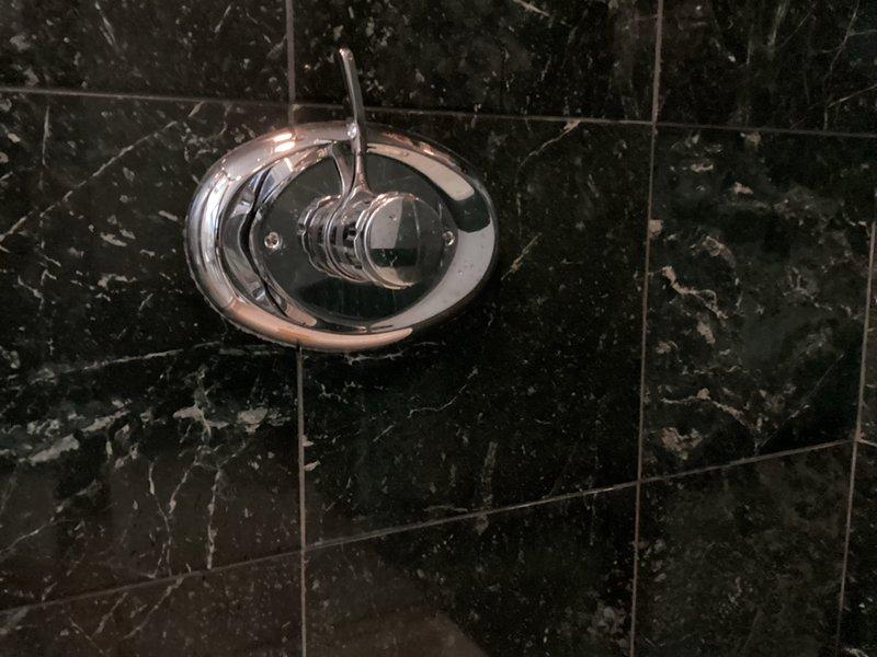 Responded to customer report of persistent leak in showerhead despite previous cartridge replacement. Inspected chrome shower control valve mounted on black marble tiled wall and diagnosed issue with valve assembly. Replaced faulty components and verified proper operation with no further leaks observed.