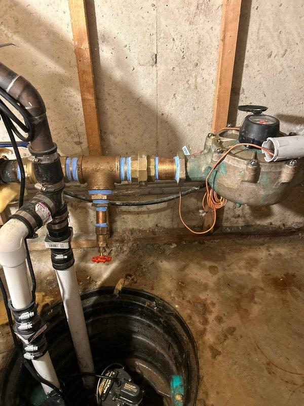 Completed installation of new plumbing assembly in utility area, including copper and PVC piping with appropriate brass fittings and valves. Installed T-junction valve assembly with ball valve and properly secured all components to the wall structure, addressing previous moisture issues as evidenced by water staining on the concrete floor.