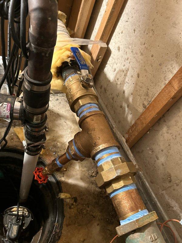 Completed installation of new plumbing assembly in utility area, including copper and PVC piping with appropriate brass fittings and valves. Installed T-junction valve assembly with ball valve and properly secured all components to the wall structure, addressing previous moisture issues as evidenced by water staining on the concrete floor.