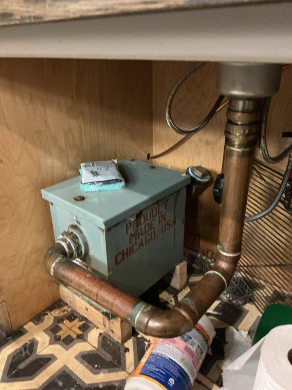 Inspected commercial grease trap systems for six kitchen units requiring cleaning service. Observed existing plumbing setup with aging copper pipes connected to a mint green pump/junction box mounted under cabinet. Documented current installation condition for accurate quote preparation on comprehensive grease trap cleaning service.