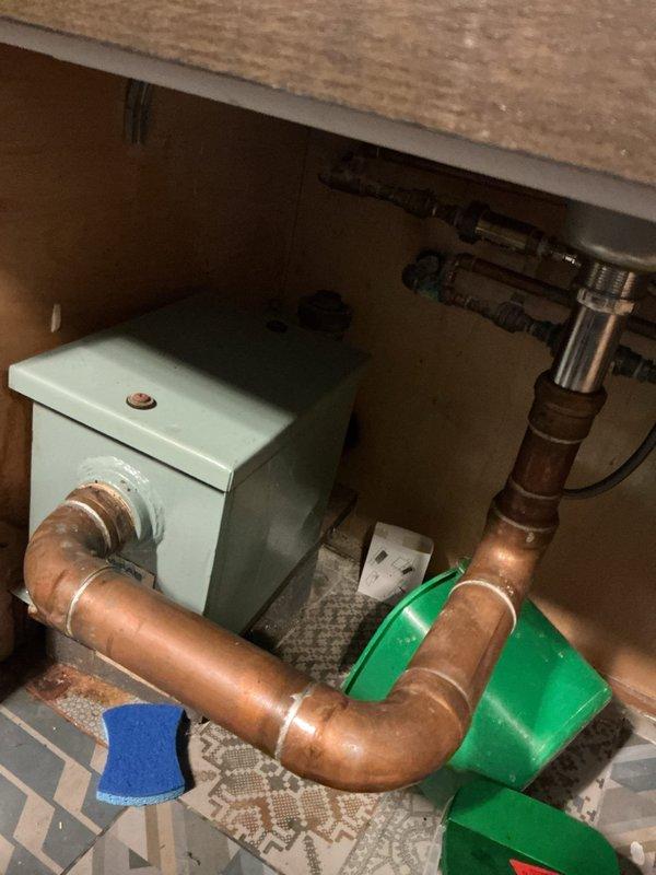 Inspected commercial grease trap systems for six kitchen units requiring cleaning service. Observed existing plumbing setup with aging copper pipes connected to a mint green pump/junction box mounted under cabinet. Documented current installation condition for accurate quote preparation on comprehensive grease trap cleaning service.