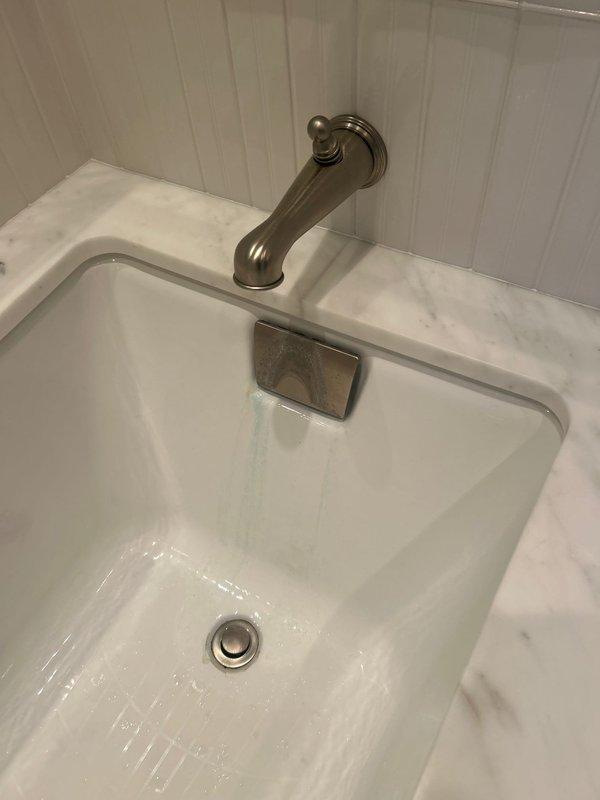 Inspected multiple plumbing issues including a kitchen pipe with a hole before the trap, a dripping pipe from basement tub, third floor tub spout diverter malfunction, toilet with abnormal refill noise, and shower handle stability problem. Documented conditions with photos of bathroom sink installation and toilet tank internal components showing aged float mechanism and potential mineral buildup requiring replacement.