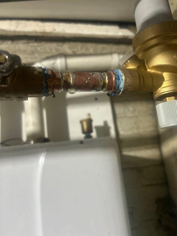 Responded to warranty service call for reported leak on tankless water heater. Upon inspection, identified previous repair work on copper pipe connections with soldered joints connecting to brass valve assembly. Visual examination of plumbing components, including copper pipes, brass valve fittings with white control knobs, and associated PVC piping showed proper installation with no active leaks detected at this time.