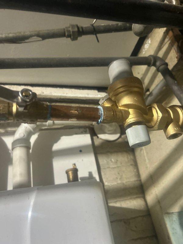 Responded to warranty service call for reported leak on tankless water heater. Upon inspection, identified previous repair work on copper pipe connections with soldered joints connecting to brass valve assembly. Visual examination of plumbing components, including copper pipes, brass valve fittings with white control knobs, and associated PVC piping showed proper installation with no active leaks detected at this time.