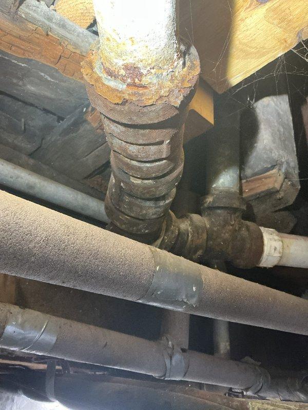 Inspected property for reported sewage odor issue persisting for several years. Identified significant corrosion and rust on vertical cast iron drain pipe in basement/crawlspace area, particularly at joint connections, which is likely the source of sewer gas infiltration. Exterior inspection revealed utility access points and drainage elements that may require further assessment.