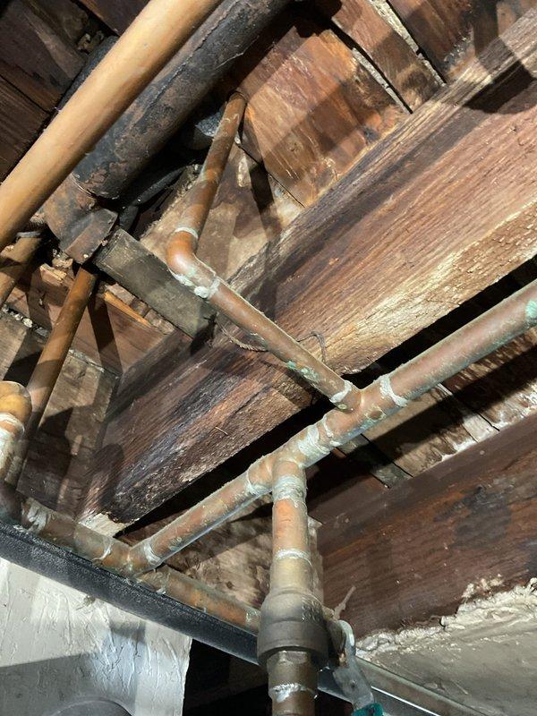 Responded to service call for bathroom sink slow drainage which resulted in sewage backup into bathtub. Upon inspection, discovered significant water damage to wooden structural elements and joists beneath the bathroom, with visible deterioration, staining, and potential rot. Examination of the copper plumbing system revealed oxidation at connection points, indicating long-term moisture exposure that likely contributed to the clog and subsequent backup issues.