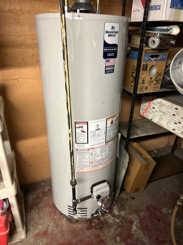 Successfully completed same day emergency installation of a Bradford White water heater in basement utility area. Installation included proper connection of copper pipes with brass fittings, installation of shut-off valves, and connection of metal exhaust vent pipe. New unit is operational with all appropriate plumbing connections secured and tested.