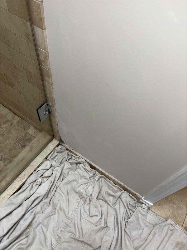 Performed inspection of suspected water leak behind shower enclosure. Removed drywall section to access the area, revealing evidence of moisture damage to wooden framing members. Documented extent of deterioration and confirmed active water intrusion in the shower corner where tiled wall meets painted drywall, likely originating from compromised waterproofing at the metal edge trim junction.
