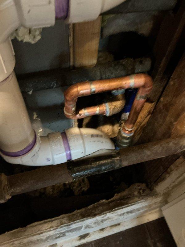 Replaced corroded copper U-bend piping assembly and installed new PVC drain components in utility area. Addressed moisture damage to surrounding wooden structural elements. Documented pre/post repair conditions with photos showing successful transition from deteriorated copper plumbing to properly sealed PVC system with appropriate joint connections.