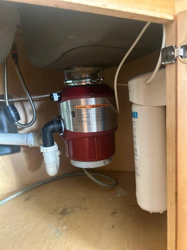 Performed comprehensive inspection of kitchen sink plumbing system in century-old residence to provide installation estimate. Examined existing garbage disposal unit, water filtration system, PVC drain pipes, P-trap assembly, and supply lines. Noted evidence of previous water damage to cabinet floor and documented current plumbing configuration for accurate replacement quote.