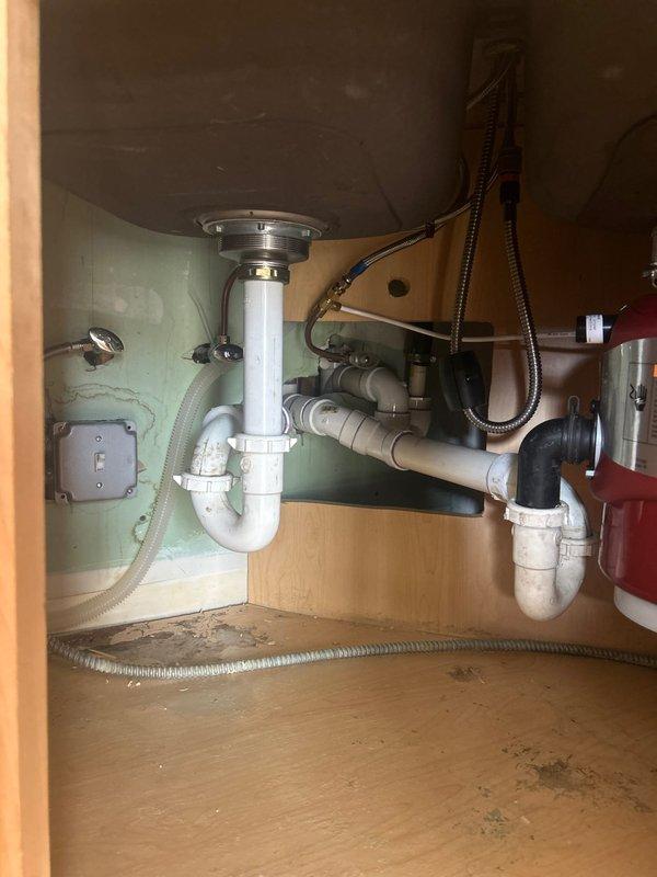 Performed comprehensive inspection of kitchen sink plumbing system in century-old residence to provide installation estimate. Examined existing garbage disposal unit, water filtration system, PVC drain pipes, P-trap assembly, and supply lines. Noted evidence of previous water damage to cabinet floor and documented current plumbing configuration for accurate replacement quote.