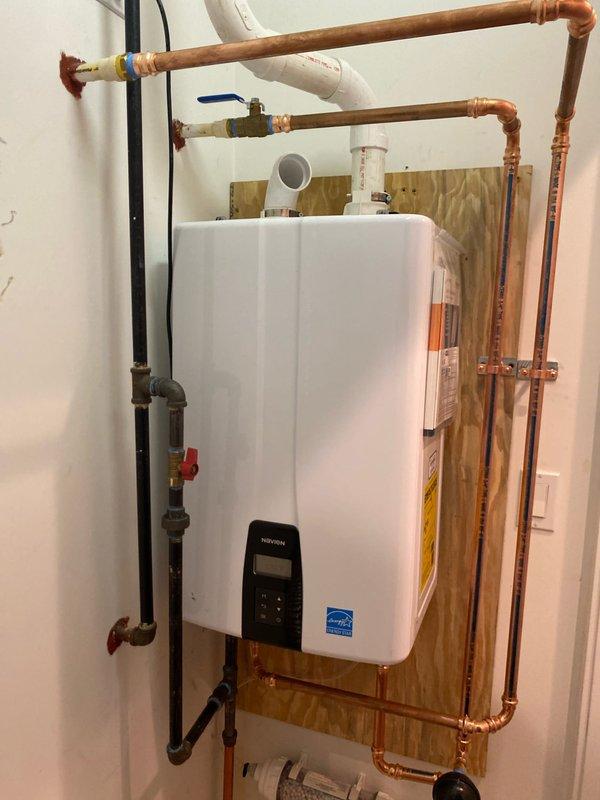 Completed installation of a new tankless water heater mounted on plywood backing with proper copper supply lines and PVC venting system. Installed shutoff valves, connected all necessary plumbing components, and verified proper operation of the unit's digital control system. Left installation area clean with manufacturer documentation attached to unit for customer reference.