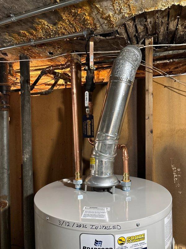 Performed complete water heater installation in basement utility area. Installed new unit with proper venting using galvanized metal pipe, connected copper supply lines, and installed shut-off valve on PVC drainage. Noted and documented significant water damage and corrosion on ceiling joists above previous unit.