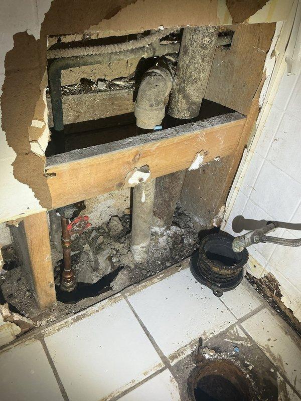 Responded to callback for bathroom plumbing issues. Upon inspection, found significant wall damage with exposed framing and deteriorated drain pipe assembly. Documented severe corrosion on brass valve and metal piping with visible deterioration in the underground access area. Took detailed photos of damage for further assessment.