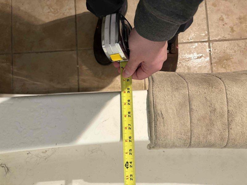 Conducted comprehensive measurements of bathtub replacement site, documenting dimensions of both the existing fiberglass tub with cracking damage and the surrounding platform structure. Measurements confirmed non-standard installation with raised platform at foot of tub requiring specialized replacement considerations. Photos taken of critical measurements to ensure accurate replacement unit specifications.