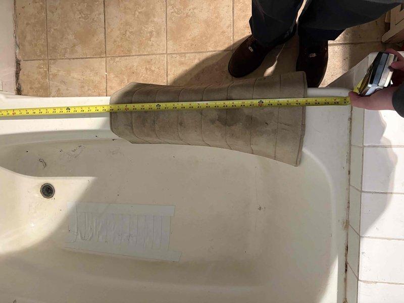 Conducted comprehensive measurements of bathtub replacement site, documenting dimensions of both the existing fiberglass tub with cracking damage and the surrounding platform structure. Measurements confirmed non-standard installation with raised platform at foot of tub requiring specialized replacement considerations. Photos taken of critical measurements to ensure accurate replacement unit specifications.