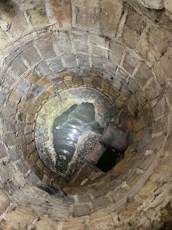 Inspected basement sewer system after customer reported sewer gas odors in basement and attic, particularly after rainfall. Identified an open drain connection without proper trapping in the basement that was allowing sewer gases to escape. Discovered significant structural deterioration in concrete surrounding the drain connection and documented a brick well structure with standing water that required remediation. Installed proper P-trap and sealed deteriorated concrete to eliminate gas escape paths.