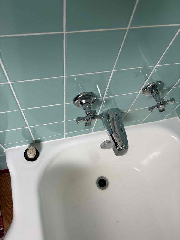 Inspected exposed plumbing system in wall access panel, documenting significant corrosion on galvanized steel pipes alongside newer PVC installation, with notable wall damage around pipe penetrations. Evaluated bathroom sink fixture with chrome faucet mounted on teal tile wall to provide comprehensive estimate for recommended repair and replacement options.