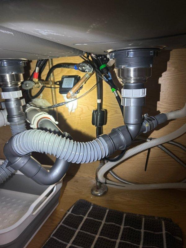 Completed installation of new sink and faucet, including proper connection of drain assembly with dual sink strainers to PVC plumbing system. Successfully installed P-trap configuration and secured all water supply lines, ensuring no leaks at connection points.