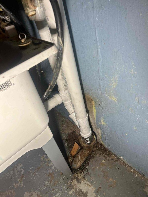 Located and inspected water leak in basement ceiling area. Identified deteriorated plumbing connections with significant moisture damage, including corrosion and mineral buildup at pipe junction points. Discovered source of leak at connection between PVC drain line and metal fitting, with visible staining on adjacent wall and floor surfaces.