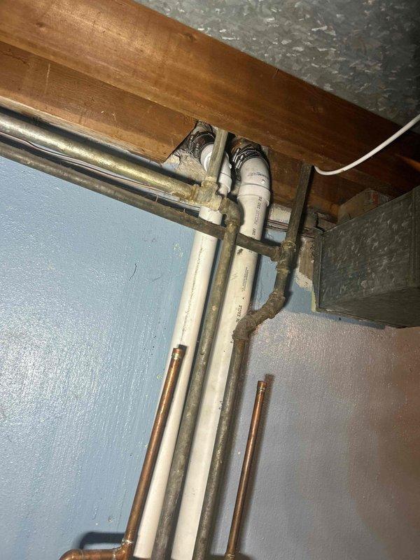 Located and inspected water leak in basement ceiling area. Identified deteriorated plumbing connections with significant moisture damage, including corrosion and mineral buildup at pipe junction points. Discovered source of leak at connection between PVC drain line and metal fitting, with visible staining on adjacent wall and floor surfaces.