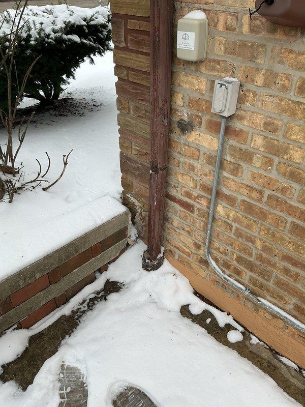 Responded to service call for water heater inspection. Examined unit and connections, confirming proper installation of the cylindrical water heater with copper pipe connections. Inspected exterior electrical components including weatherproof outlet box and utility connection on brick exterior wall.