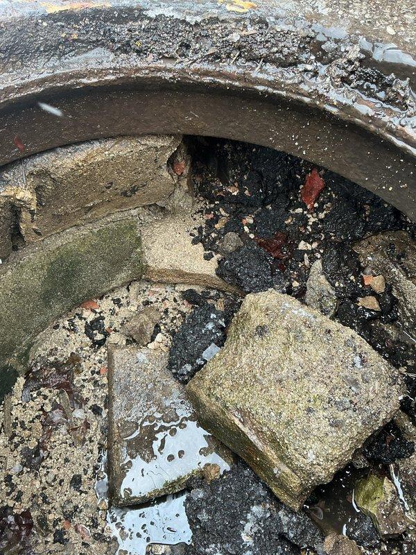 Responded to service call for manhole filled with debris. Upon inspection, discovered significant accumulation of construction waste including concrete blocks, stone fragments, and sand causing complete blockage. Standing water was present with visible algae growth on interior walls indicating prolonged moisture exposure and drainage issues.