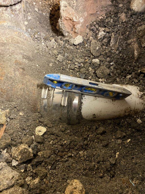 Completed underground pipe repair by replacing corroded metal fitting connected to PVC line. Installed new coupling with proper leveling to ensure horizontal alignment, addressing water flow issues in basement/crawlspace area.
