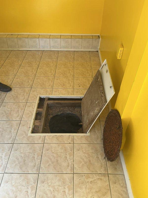 Performed camera inspection of catch basin/man hole accessed through floor hatch. Documented significant concrete deterioration and visible cracks in the basin walls, with standing water and sediment accumulation at the bottom. Noted structural wear and a potential drainage opening in the upper portion of the circular structure requiring attention.