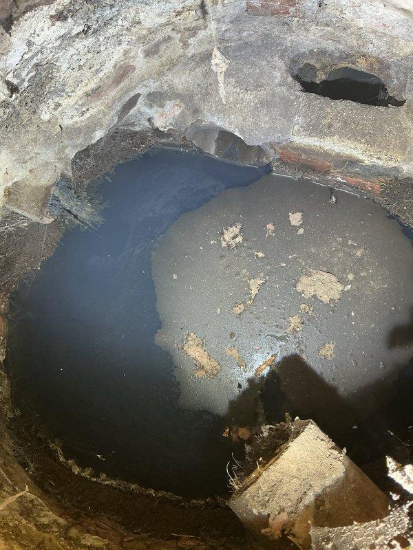 Performed camera inspection of catch basin/man hole accessed through floor hatch. Documented significant concrete deterioration and visible cracks in the basin walls, with standing water and sediment accumulation at the bottom. Noted structural wear and a potential drainage opening in the upper portion of the circular structure requiring attention.