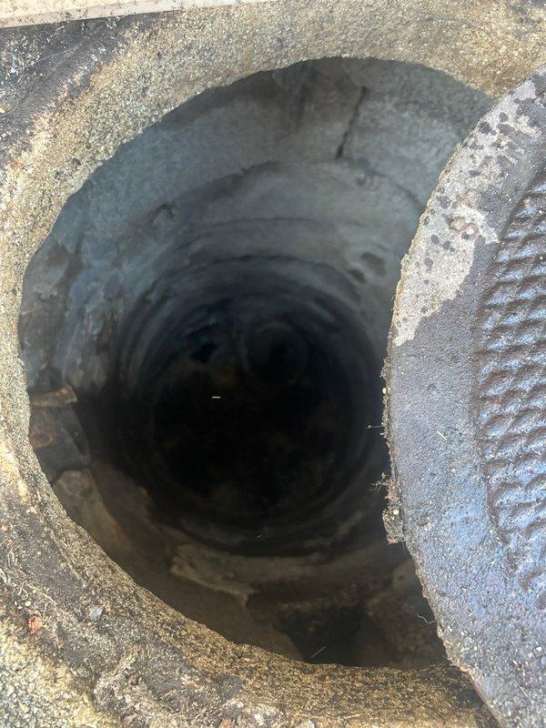 Performed scheduled grease trap cleaning service at exterior location. Accessed drainage system through circular metal grate set in concrete collar amid brick pavers. Inspected vertical concrete shaft for proper flow and functionality before completing maintenance procedure.